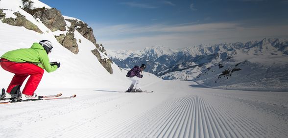 Skifahrer in der Abfahrtshocke unterwegs Richtung Tal auf frisch gespurter Piste